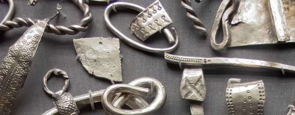 Various pieces of silver objects are laid out on a grey cloth.